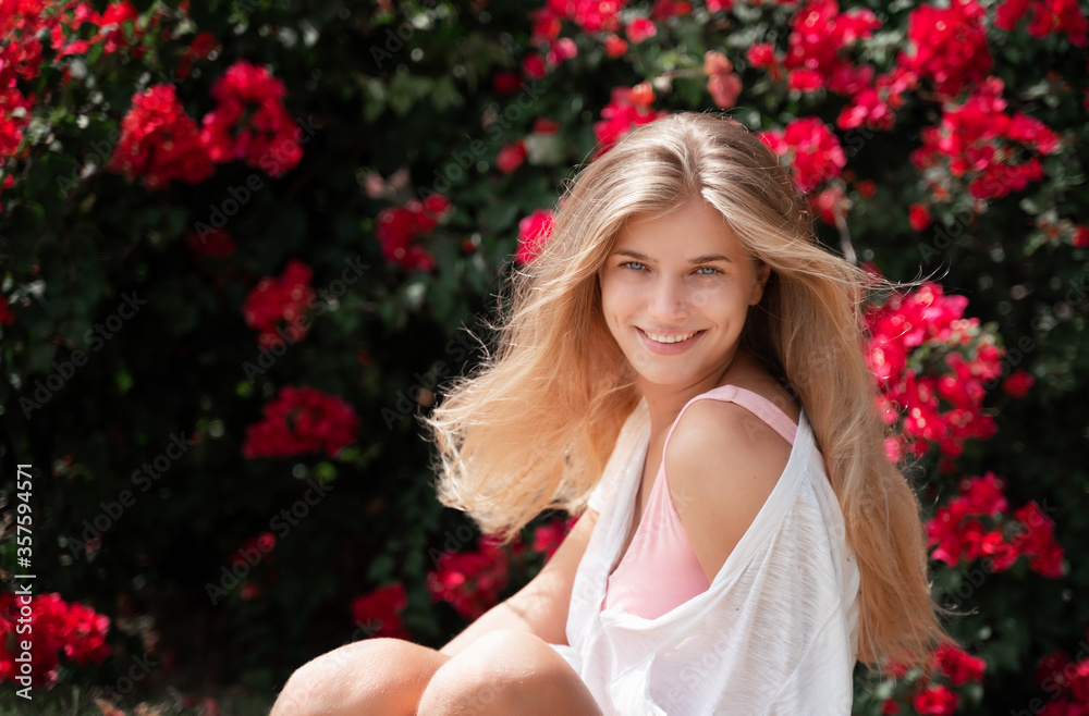 Beautiful young blonde with long hair and blue eyes and a charming smile in a pink flowered garden, beauty and nature concept