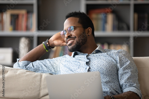 African guy distracted from using laptop do remote work daydreams looking at window feels calm inner harmony enjoy fresh air and lazy day. American relaxed man spend free time with pc at home concept