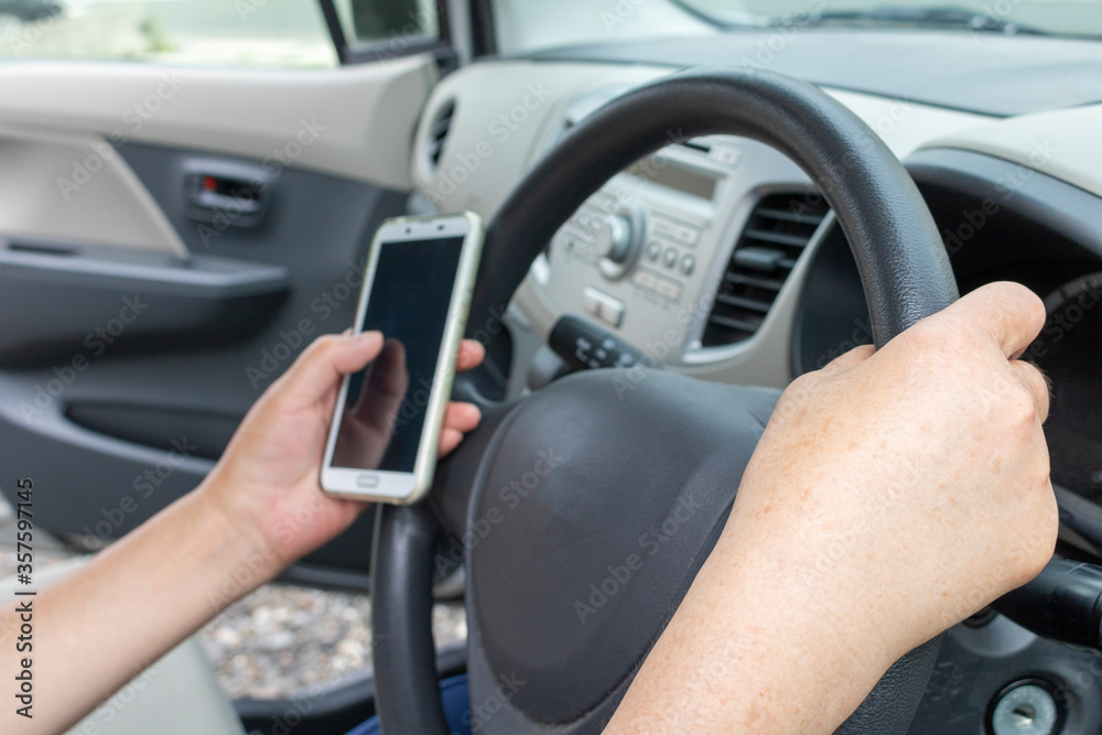 停車中に運転席でスマートフォンを操作するシニア女性 停車中に運転席でスマートフォンを操作するシニア女性
