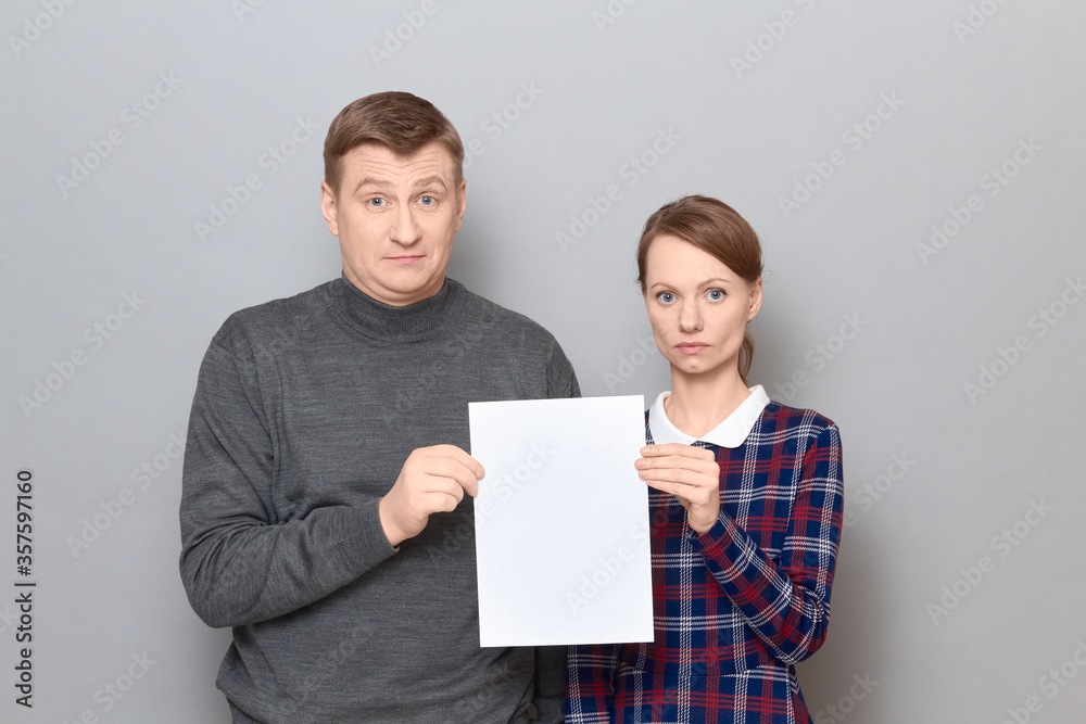 Portrait of adult couple holding together white blank paper sheet Portrait of adult couple holding together white blank paper sheet