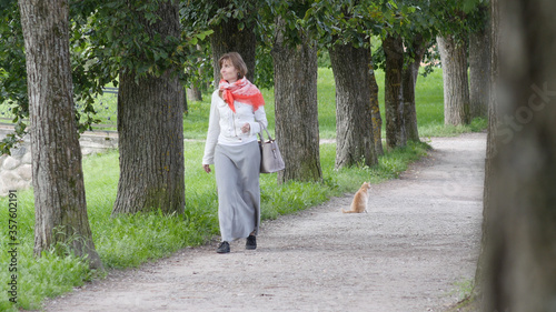 Happy woman in a dress and red scarf walking on green trees alley in park