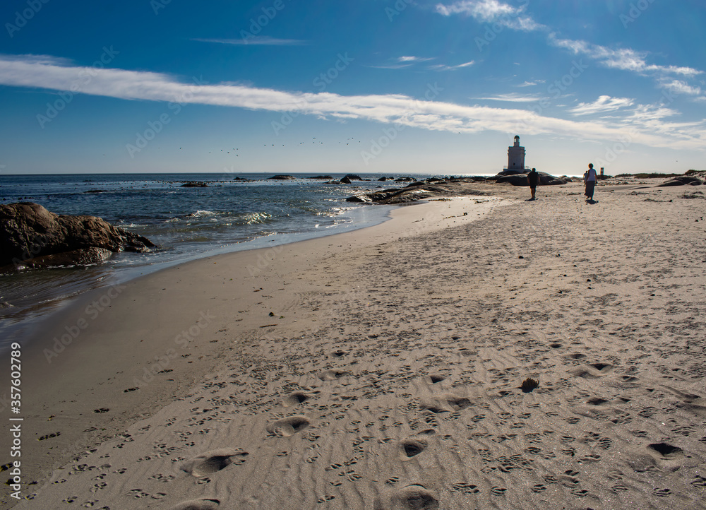 People walking along the beach with a lighthouse in the background.