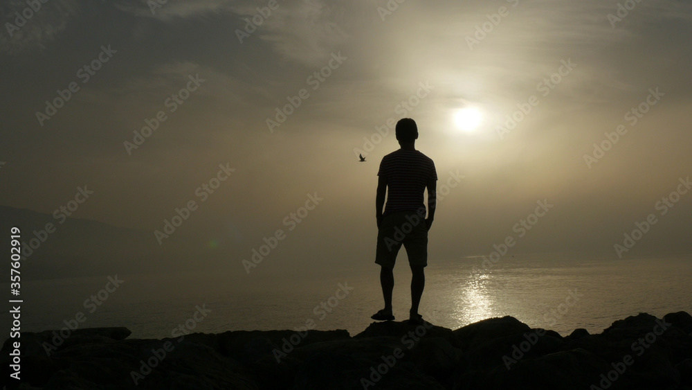 Silhouette of young man looks at sunrise and reflection of sun on sea water in Marbella area, Spain