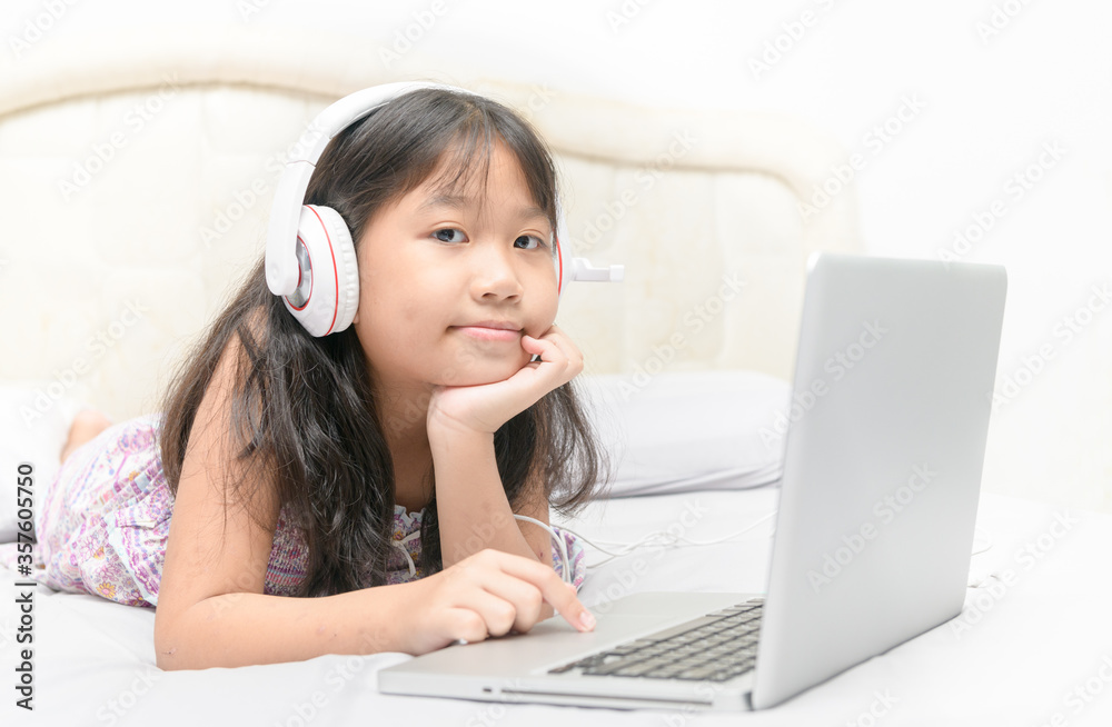 Happy cute girl lying and wearing headphones to learn online from a laptop Happy cute girl lying and wearing headphones to learn online from a laptop