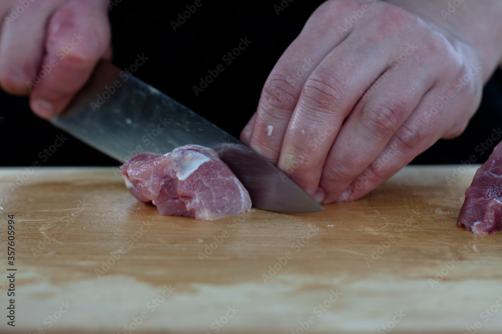 cutting meat into pieces with a knife on a wooden Board. the cook cuts the meat.