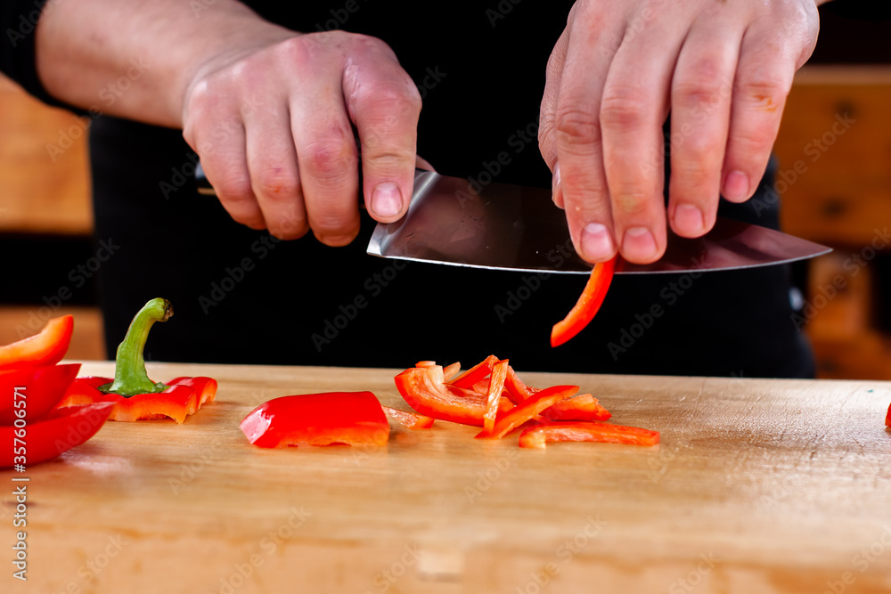 the cook slices red peppers on a wooden Board