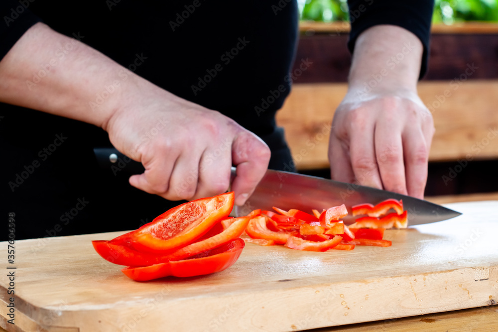 the cook slices red peppers on a wooden Board the cook slices red peppers on a wooden Board