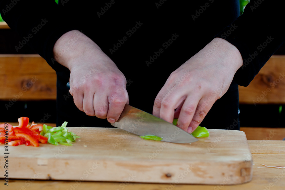 the cook cuts green peppers into strips on a wooden Board