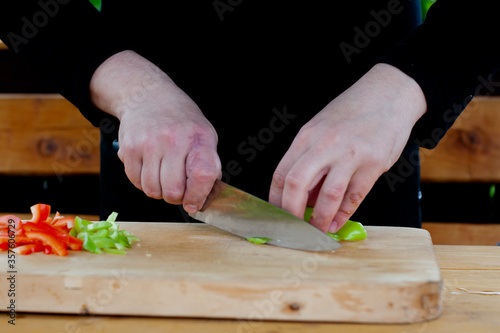 the cook cuts green peppers into strips on a wooden Board