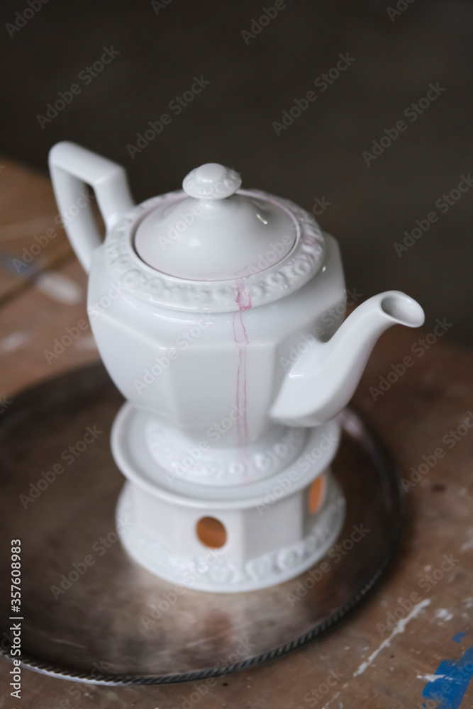 White teapot with red spots on portable hearth in artist workshop