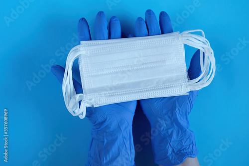 Two hands of a Doctor in medical gloves holds, takes, gives medical surgical masks for covering the mouth and nose. Top view, close up, on blue background