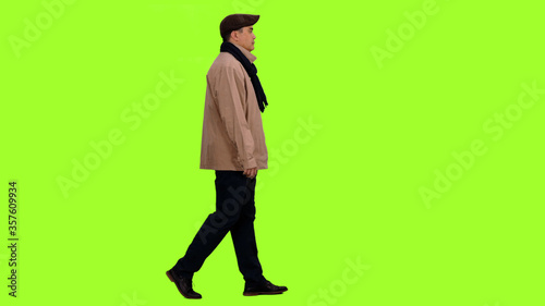 Fotografie Elegant man in jacket with scarf and flat cap walking on green background, Side