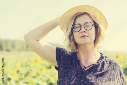 Portrait of happy mature woman with hat enjoying of freedom in the sunflowers field