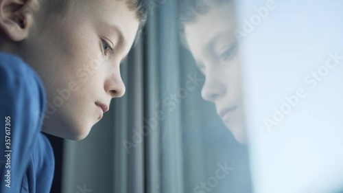 Sad unhappy kid standing near the window. Upset boy.