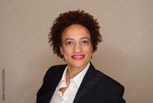 portrait of a black business woman smiling confidently and wearing a dark suit and white shirt. 
