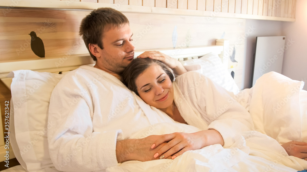 Portrait of happy smiling woman hugging her husband lying in bed at hotel room Portrait of happy smiling woman hugging her husband lying in bed at hotel room