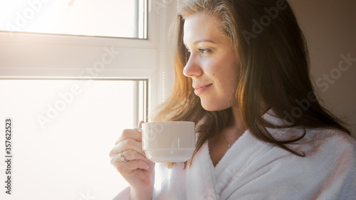 Portrait of smiling woman drinking coffee and looking out of the window at morning