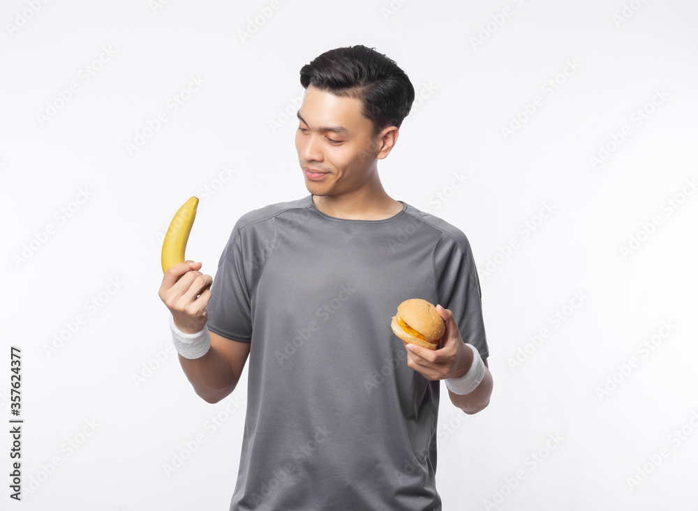 Young handsome asian sport man holding banana and hamburger with smiling isolated on white background. Young handsome asian sport man holding banana and hamburger with smiling isolated on white background.