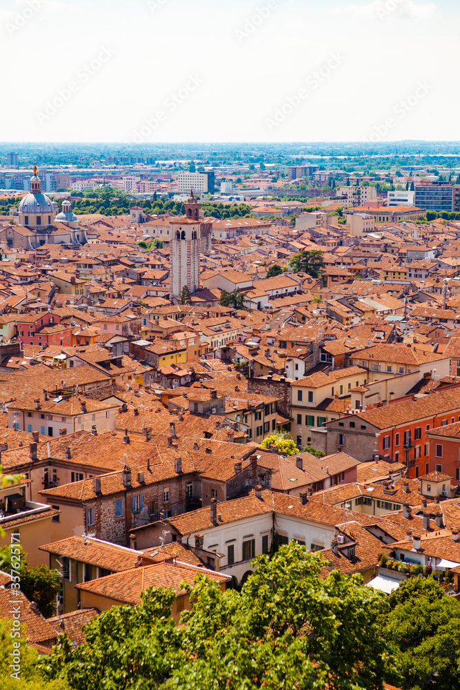 Aerial view of the historical center of Brescia (Lombardy, Italy) with tiled red roofs, chimneys, cathedral's domes and tall white brick old towers. Traditional European medieval architecture. 