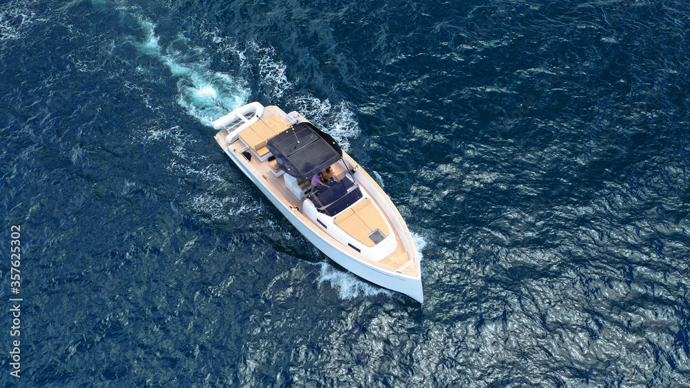 Aerial drone top down photo of small power boat with wooden deck cruising in deep blue Mediterranean sea
