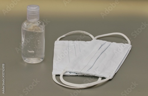 Two white fabric face masks and a bottle of sanitizer to protect people from getting an illness like influenza or corona