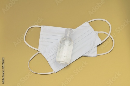 Two white fabric face masks and a bottle of sanitizer to protect people from getting an illness like influenza or corona