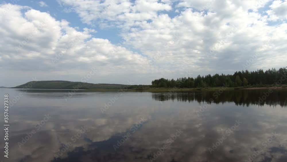 A peaceful summer day with white clouds on a blue sky. Water is still and barely moves, giving a perfect mirrored reflection of the sky. Green and lush forest in the background. A peaceful summer day with white clouds on a blue sky. Water is still and barely moves, giving a perfect mirrored reflection of the sky. Green and lush forest in the background.