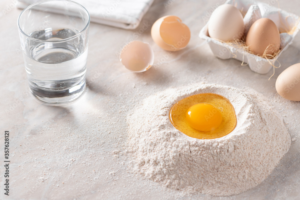 pile of whole grain flour with an egg, a glass of water, eggs and eggshells on the kitchen table. Cooking process. horizontal image. selective focus. place for text pile of whole grain flour with an egg, a glass of water, eggs and eggshells on the kitchen table. Cooking process. horizontal image. selective focus. place for text