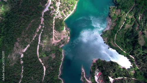 Bird-eye view flying above lake Tsivlou in the mountains of Peloponnese in Greece. Green hills surrounding turquoise water with reflection of clouds and bright sunlight photo