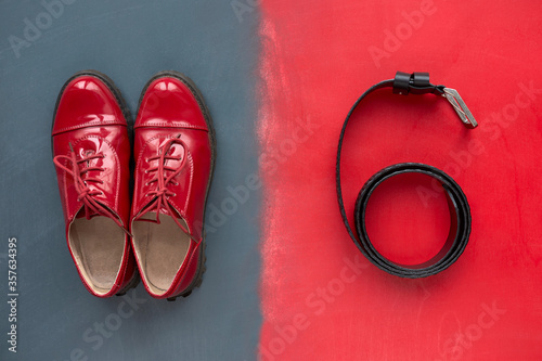 Fashionable concept. Top view of classic red patent leather shoes and black leather belt for trousers on red and grey background.