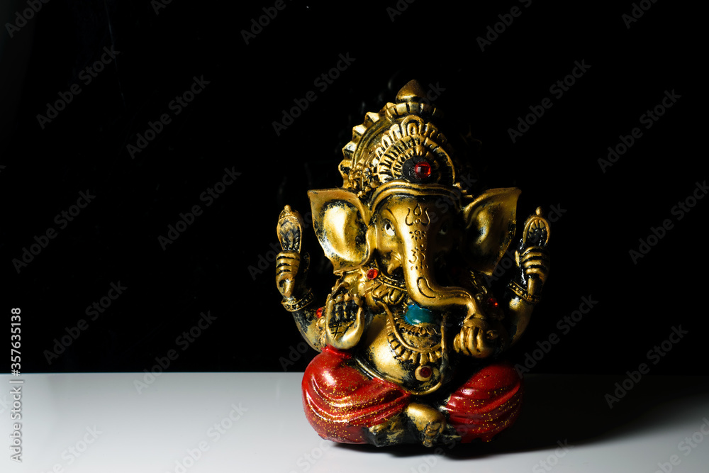 An isolated sculpture of the Indian god Ganesha placed on a reflective white table in a dark background