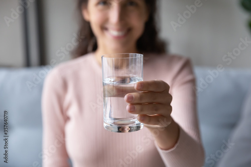 Close up smiling young woman holding glass of pure mineral fresh water in hand, happy girl offering glass to camera, healthy lifestyle and good daily habit concept, natural beauty and nutrition
