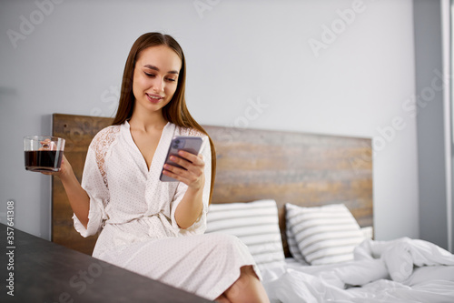 young caucasian female begins her morning from coffee and smartphone, she is checking all news and chatting with friend in the morning. sits in bathrobe at home