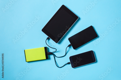 Tech Device Charge Sharing  two mobile phones and tablet charging from one powerbank battery charger. Flat lay  top view on blue background