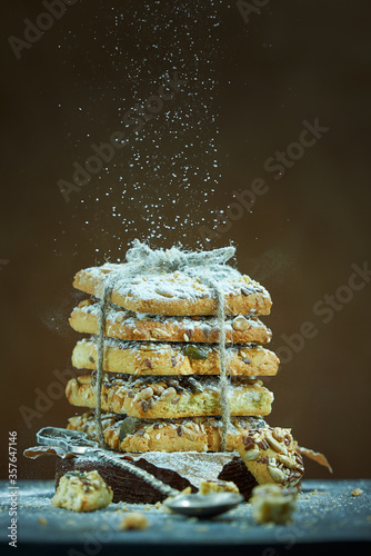 Square cookies with nuts and seeds are sprinkled with powdered sugar on a brown background. Photo with copy space.