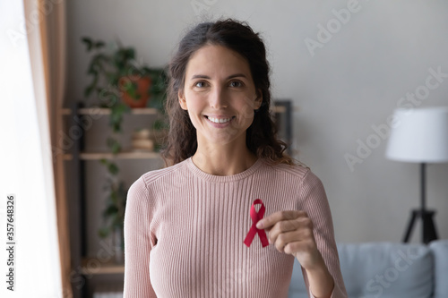 Head shot portrait smiling young woman holding awareness red ribbon, symbol of fight against AID, HIV, cancer, drugs addiction, supporting people with disease, regular checkup promotion