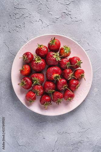 Fresh ripe strawberry fruits in pink plate, summer vitamin berries on grey stone background, top view