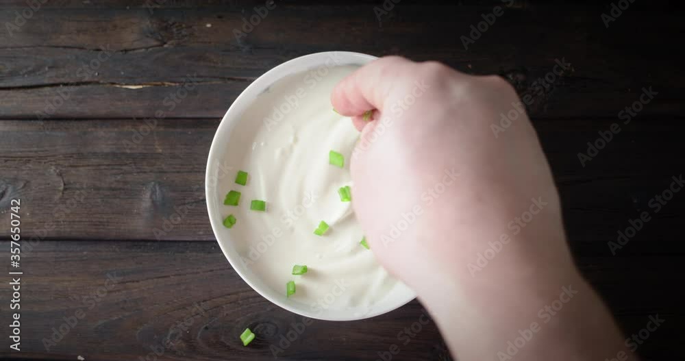 Men's hand throws chopped green onions into sour cream. Men's hand throws chopped green onions into sour cream.