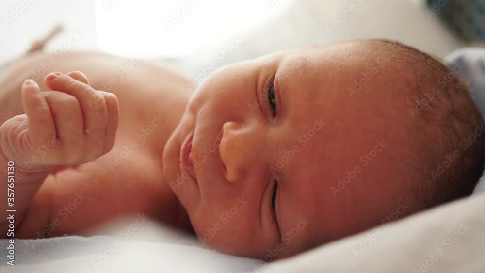 Portrait of a newborn baby lies on a blue bedspread and touches his lip with his tongue. Without clothing. First moments of life. Close-up of newborn baby face portrait Portrait of a newborn baby lies on a blue bedspread and touches his lip with his tongue. Without clothing. First moments of life. Close-up of newborn baby face portrait