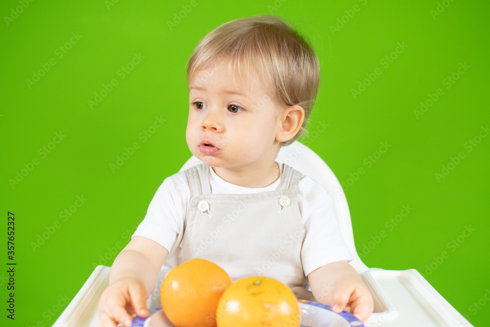 Blond baby sitting in the high chair with oranges in his hands Blond baby sitting in the high chair with oranges in his hands