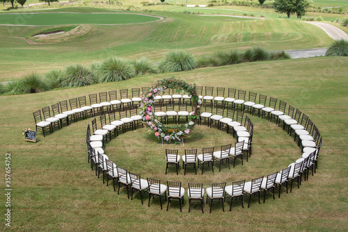 Unique round spiral chair pattern wedding ceremony setting at rolling hills countryside with brown chiavari chairs and white cushions photo