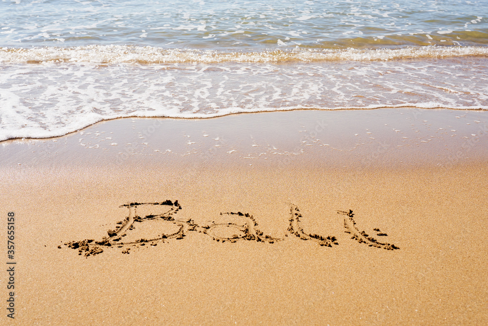 Bali inscription on a tropical sandy beach with waves and foam on a background. Bali inscription on a tropical sandy beach with waves and foam on a background.