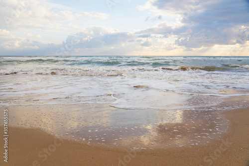 Fototapeta Naklejka Na Ścianę i Meble -  Sandy beach on a sunset with reflection on wet sand and waves with foam. Copy space.