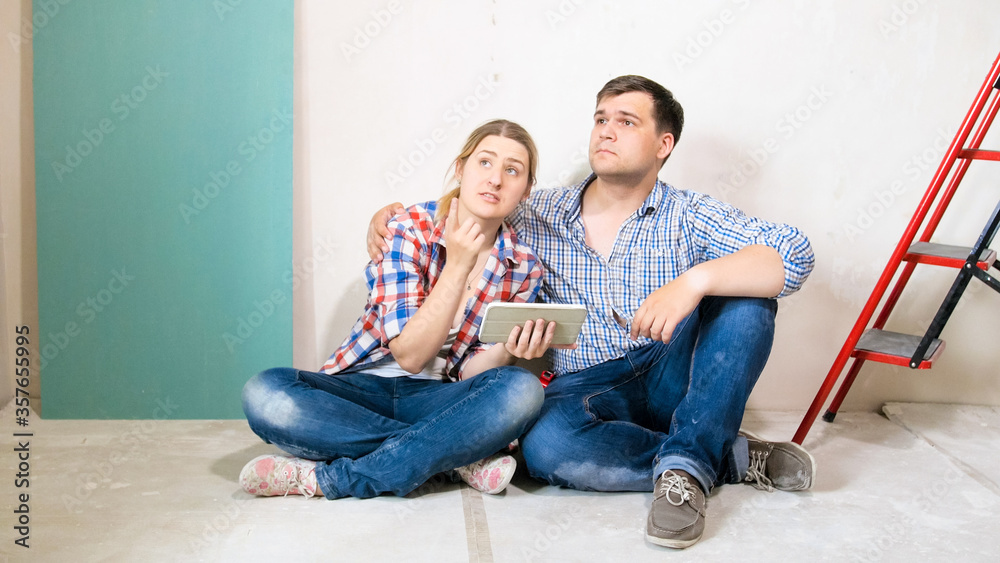 Smiling young couple choosing design for their new house on tablet computer Smiling young couple choosing design for their new house on tablet computer