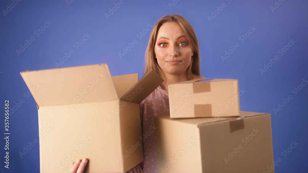 Young caucasian woman with packed cardboard boxes and surprised face isolated on the blue background. Copy space. Young caucasian woman with packed cardboard boxes and surprised face isolated on the blue background. Copy space.