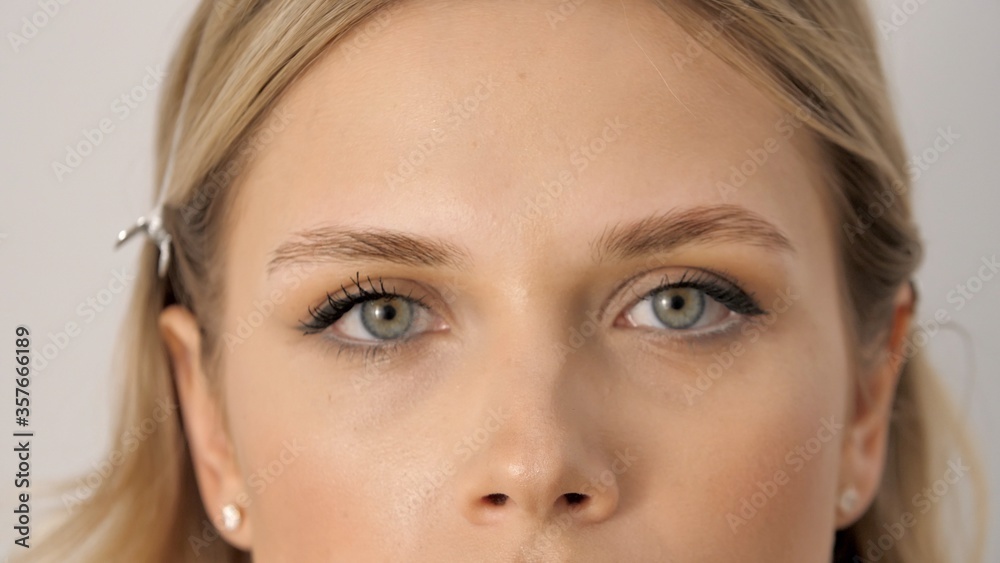 Fototapeta premium Portrait of a young beautiful well-groomed woman or lady looking in a frame. Eyes of a adult blonde girl with makeup look in a camera. Attractive female face. Successful business woman