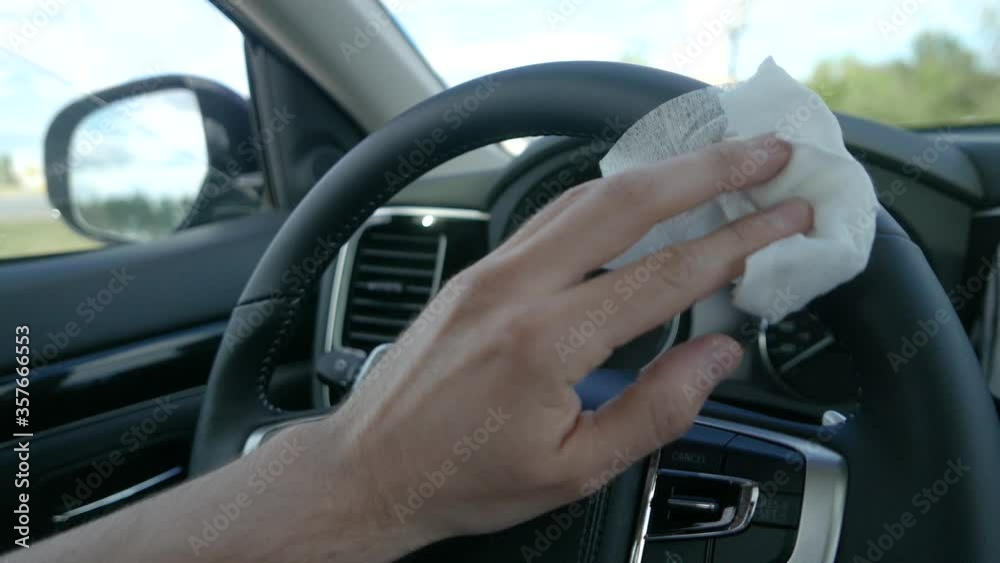 Driver using a disinfecting antibacterial wipe, to sanitize the wheel of his car vehicle closeup Driver using a disinfecting antibacterial wipe, to sanitize the wheel of his car vehicle closeup