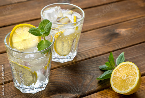 Two glass with lemonade or mojito cocktail with lemon, mint and ice over rustic wooden background.