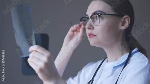 Female doctor is surprised holding X-ray of lungs, fluorography, roentgen in hospital. Woman in medical gown, stethoscope in consulting room. Medicine concept. photo