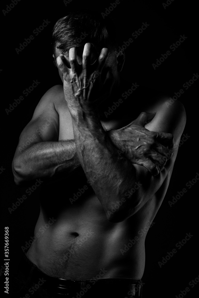 The man covers his face with his hands. Regret or fear. On dark background. Black and white photo. Depression, pain, loneliness, self-isolation. The man covers his face with his hands. Regret or fear. On dark background. Black and white photo. Depression, pain, loneliness, self-isolation.